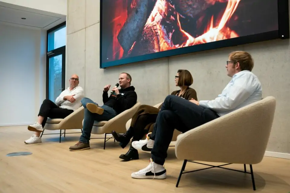 Vier Personen in Sesseln vor Screen mit Kaminfeuer